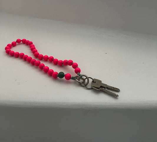 upbeads wooden bead chain used as a keychain the color is bright neon pink with a signature bead in sage green